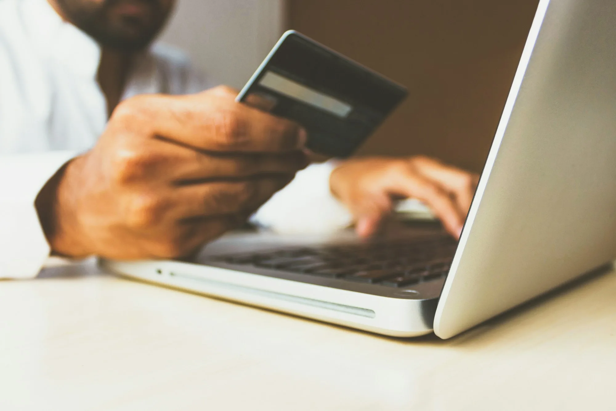 Hand holding a payment card while shopping online on a laptop