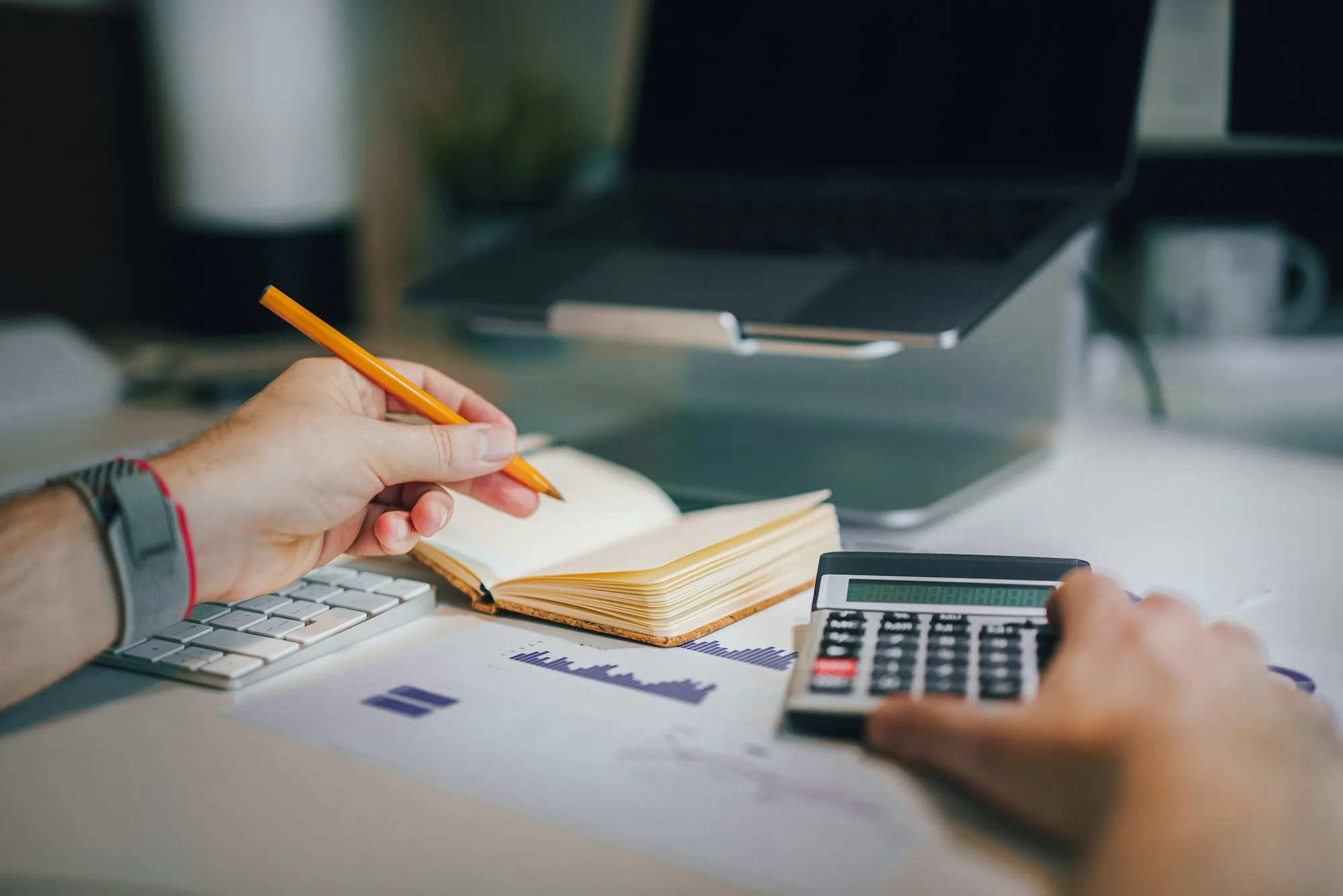 Hands working out a budget with a calculator and pencil next to printed charts