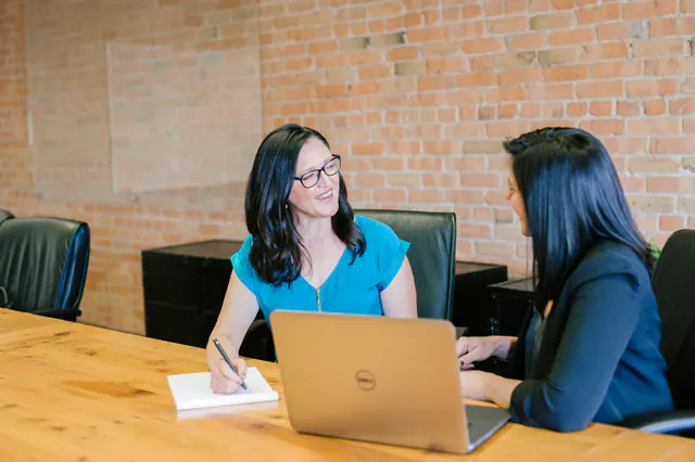 Two colleagues talking through a report in a meeting with a laptop